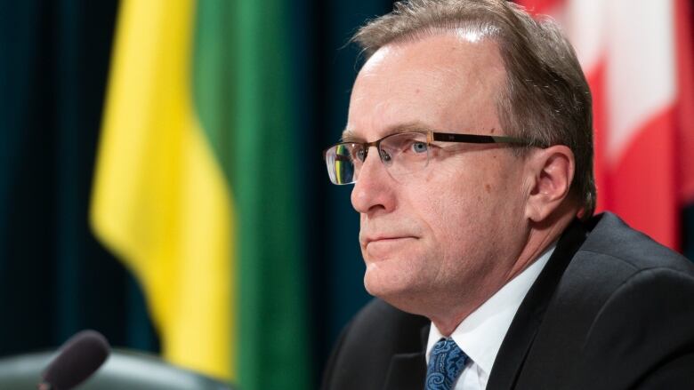 Man Speaking at a press conference with the Canada and Saskatchewan Flag behind him