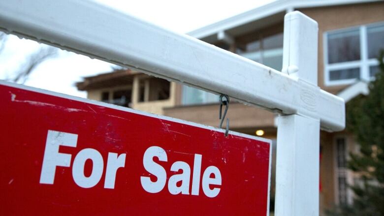 A red for sale sign is pictured in front of a property in the background. 