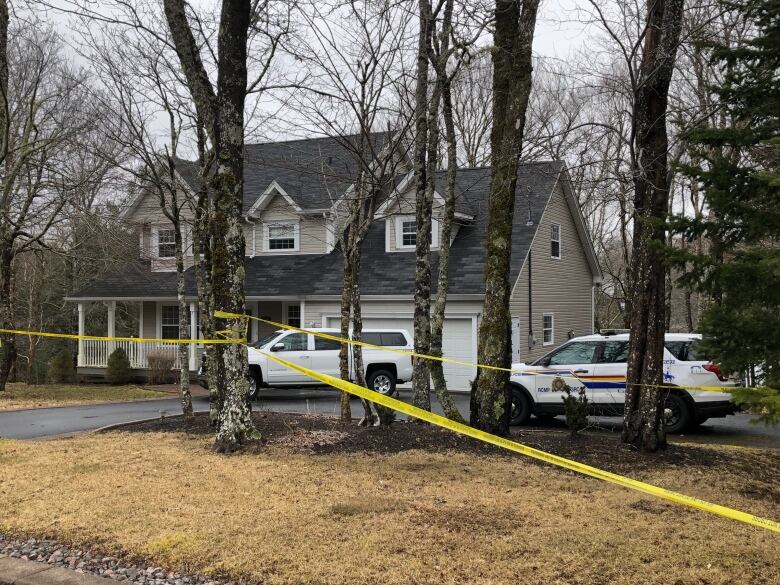 A large home with yellow police tape around it. Two police vehicles are seen in the driveway.