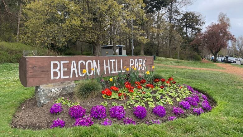 A wooden sign reading Beacon Hill Park sits above a flower bed in a public park.