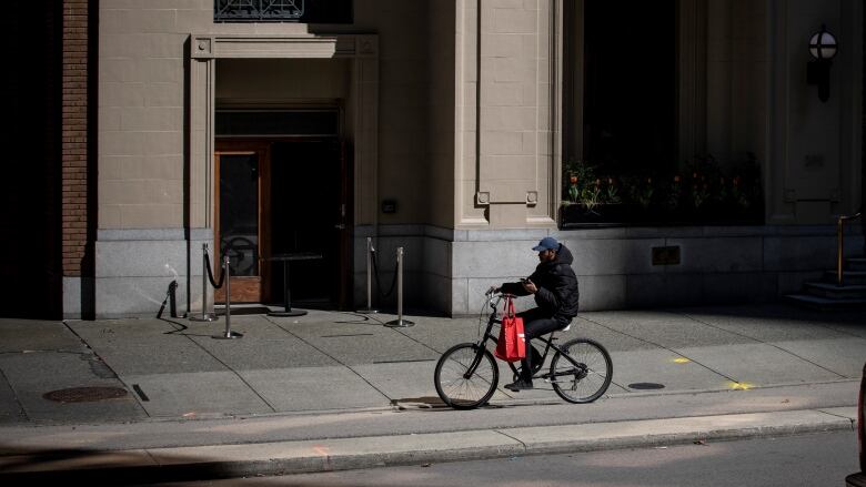 A food delivery worker rides a bike on a pavement.