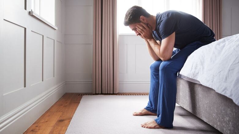 A man sits on the edge of a bed.