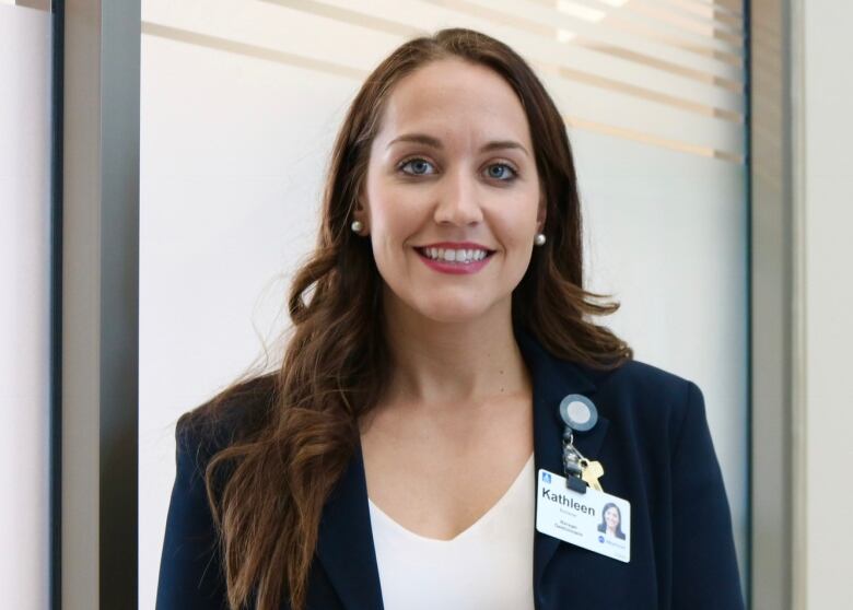 A woman wearing an ID badge on her blazer stands in front of a frosted glass window