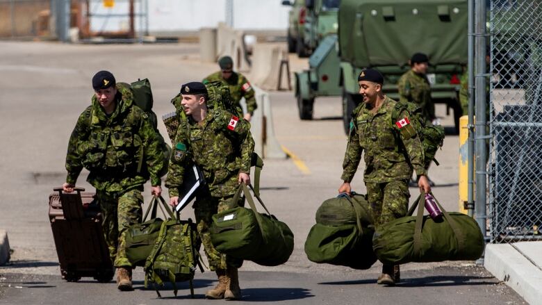 Troops in green uniforms carry duffel bags. 