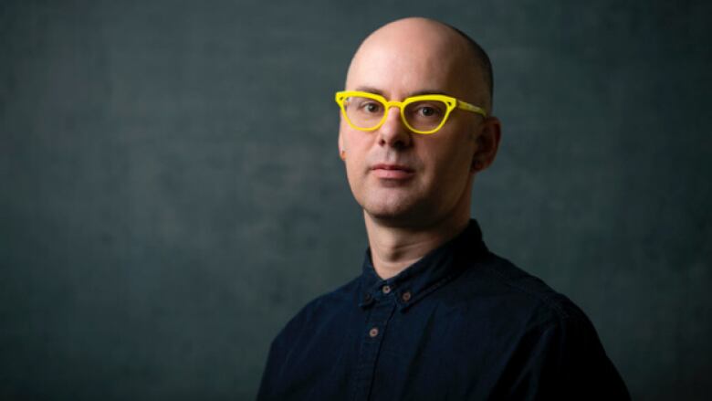 a portrait of a bald white man with bright yellow glasses.