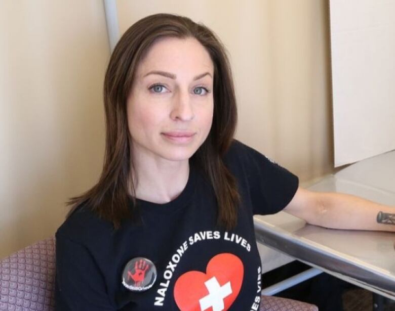 A woman with brown hair wear a black t-shirt that says Naloxone saves lives