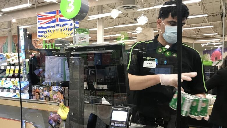 A cashier at a grocery store wearing a mask. 