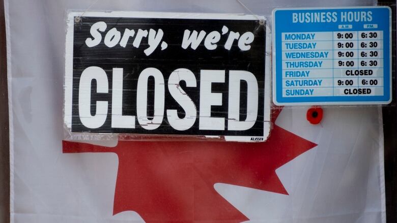 A closed sign and hours rests in front of a Canadian flag.