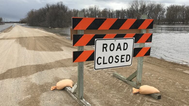 A temporary road-closed sign stands on a provincial road in Manitoba. Flood water from the Red River surrounds each side of the road.