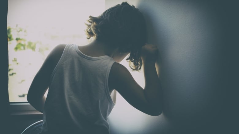 A child with curly hair sits in a window. The child is turned away from the camera.