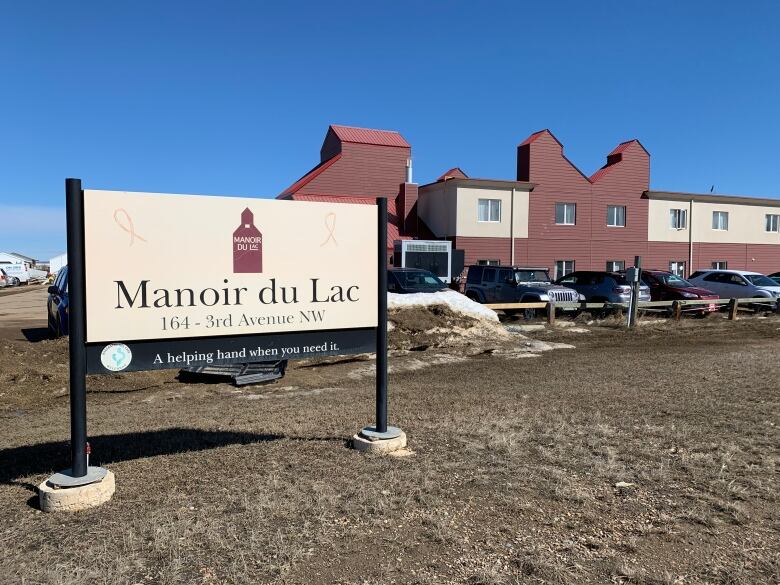 A red brick building with a small parking lot in front. A sign in front of the property reads, Manoir du Lac.