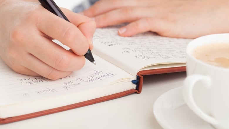 Hands writing in leather bound journal or diary with coffee.