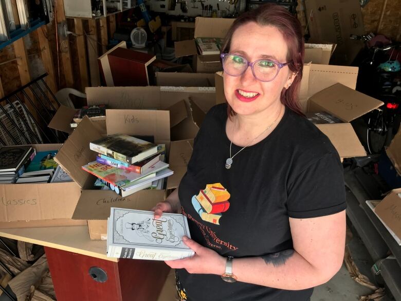 A red-haired woman in a black shirt opens boxes of books.