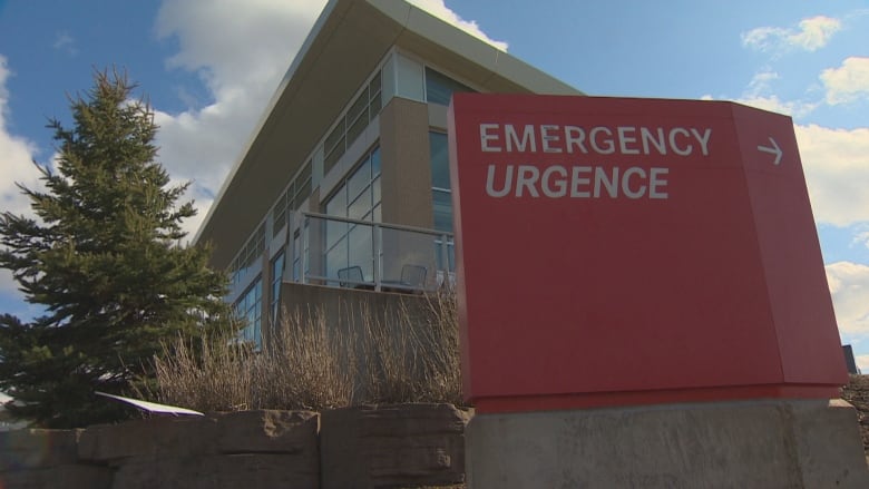 A large red sign with white lettering says emergency with an arrow pointing around a building.