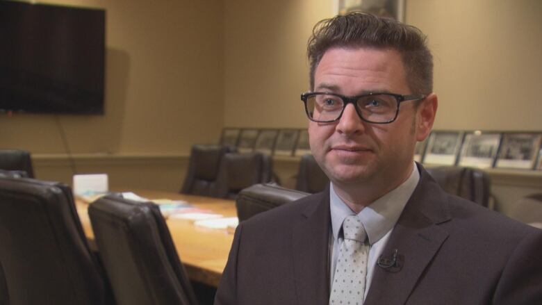 Man with glasses in suit stands in empty boardroom