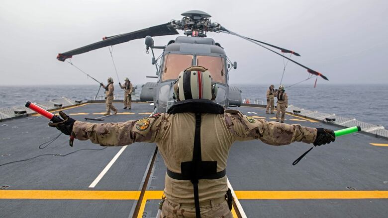 Ground crew store a military helicopter on the deck of a frigate.