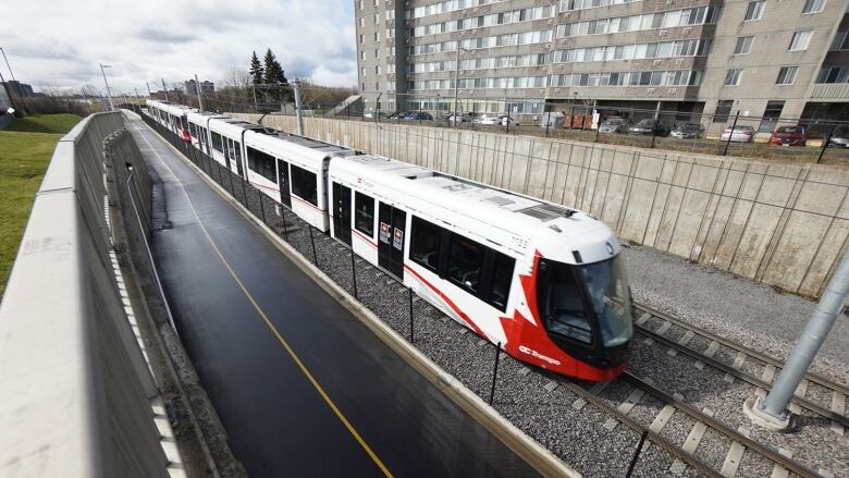 A red and white public transit train on a track near a highrise.