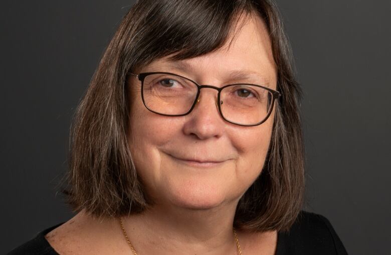 A woman with chin-length brown hair and glasses smiles at the camera.