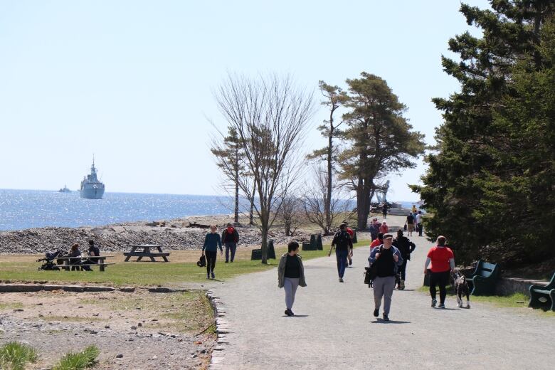 Pedestrians enjoy a sunny day by walking through Point Pleasant Park. The water can be seen in the background.