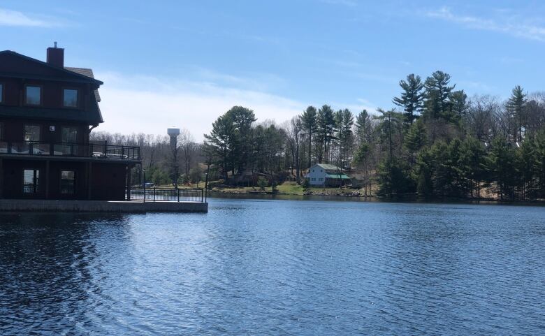 Cottages are seen on a lake on a sunny day. There are two cottages, one in foreground, one in background