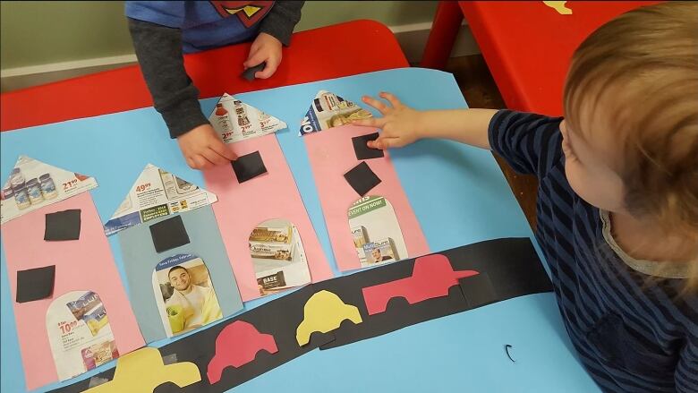 Two children in daycare play with coloured cutouts.