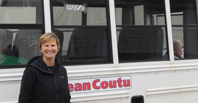 A woman stands in front of an old white schoolbus.