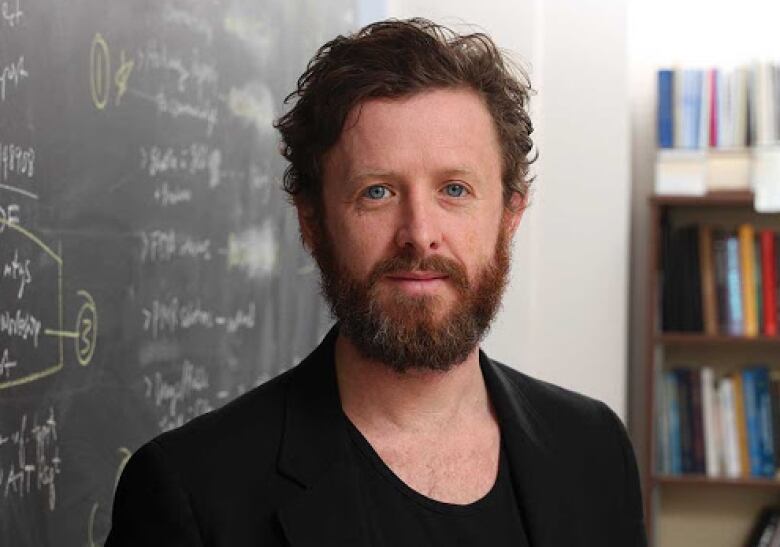 Bearded man standing in front of a chalkboard.