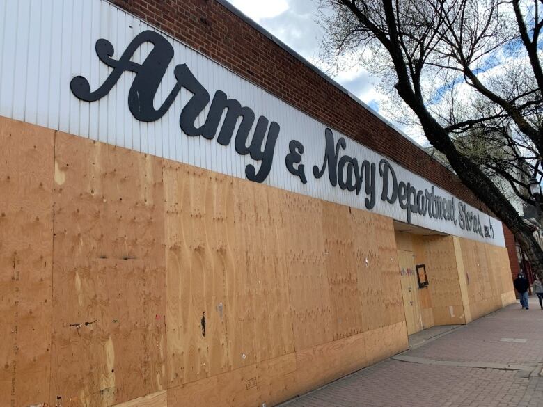 A view of a storefront from outside, on the sidewalk. The windows are boarded up with plywood.