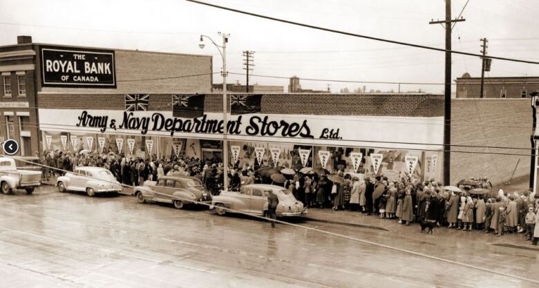 A historical photo in sepia tones showing people lined up on the sidewalk to enter the Army & Navy department store.