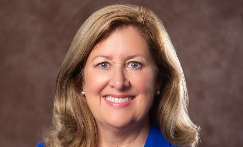 A professional portrait of a woman with long light brown hair, wearing a royal blue blazer over a black shirt. 