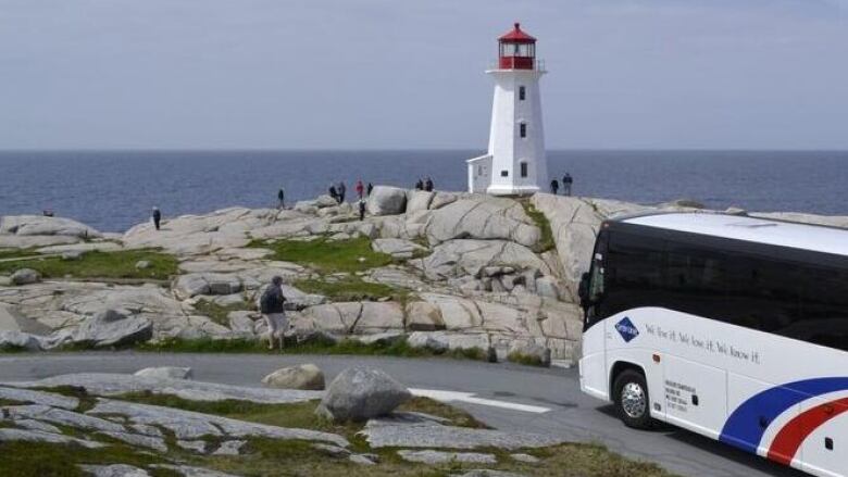 A large white tour bus parked outside the Peggys Cove Lighthouse.