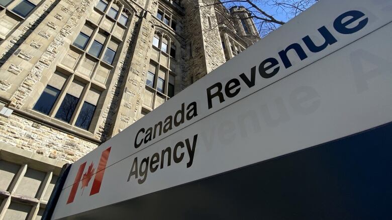 A sign reading 'Canada Revenue Agency' stands outside of a large stone building. 