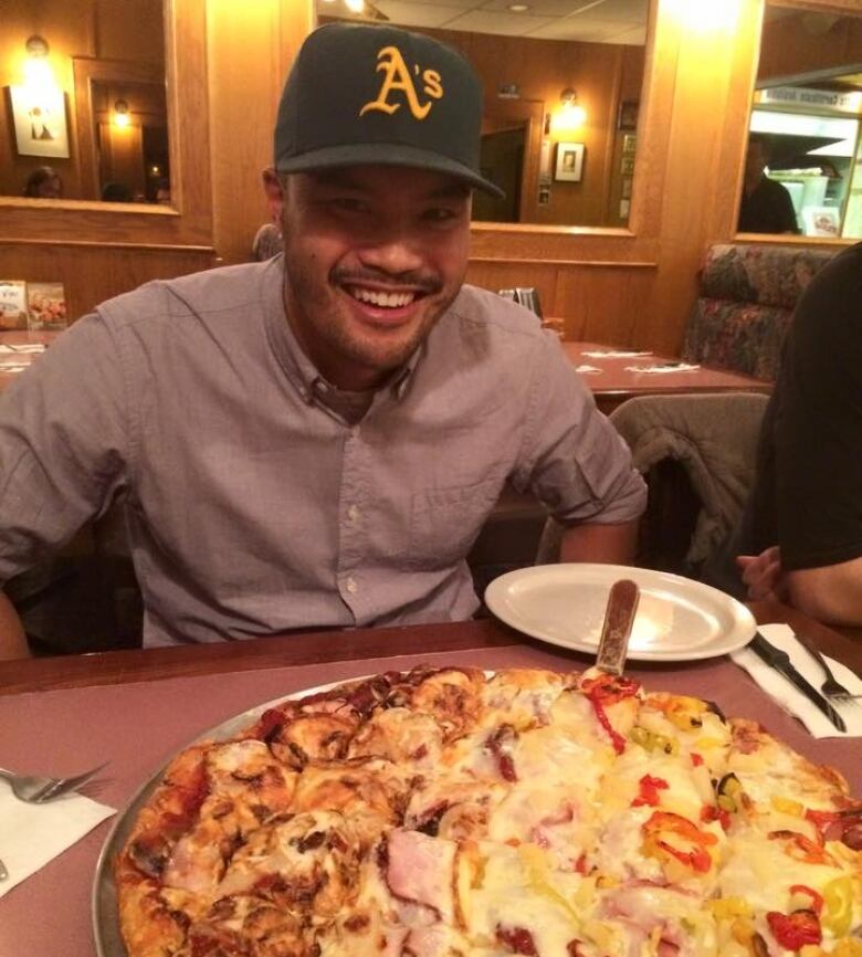 A man sitting at a table with a large pizza in front of him.