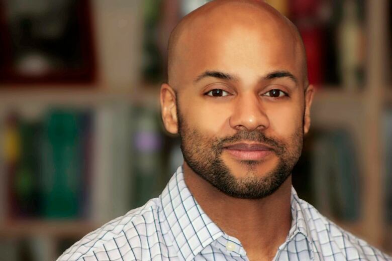 A closeup of a man with a beard and a shaved head, in front of a blurred background.