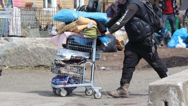 A person is seen pushing a cart filled with belongings through a rundown area.