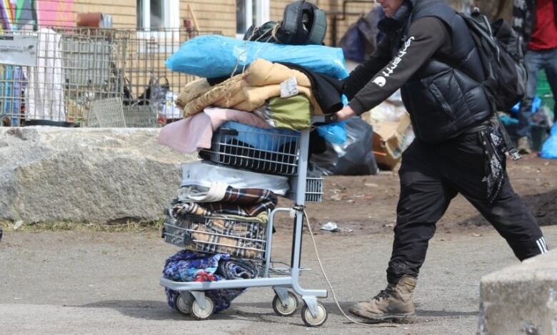 A person is seen pushing a cart filled with belongings through a rundown area.