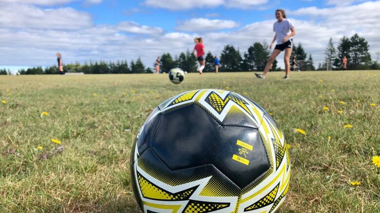 A soccer ball sits on a field with kids in the background.