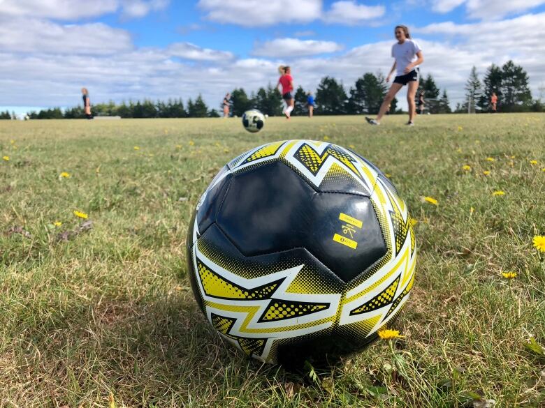 A soccer ball sits on a field with kids in the background.