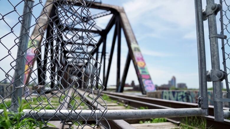 A hole in a fence in front of an old railway bridge.