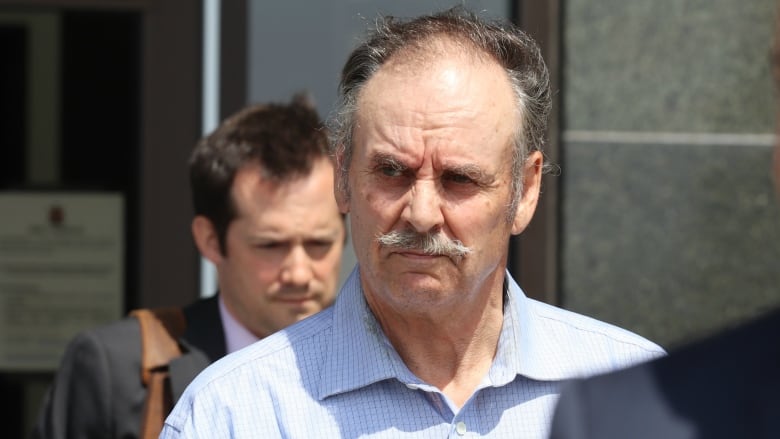 A man with a receding hairline and a moustache exits a building. 