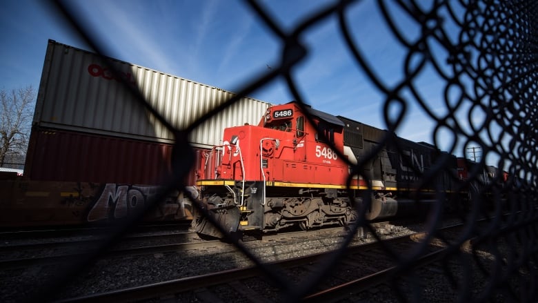 A train can be seen behind a chain-link fence. It is a file photo.