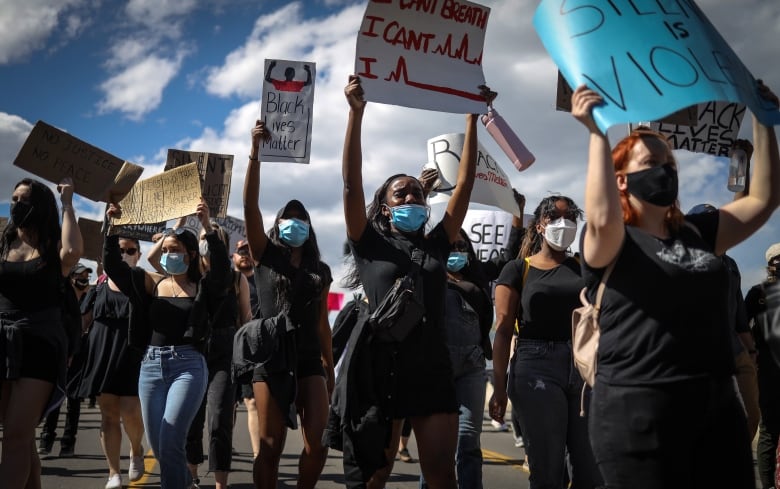 A group of masked protester hold up signs, on saying 