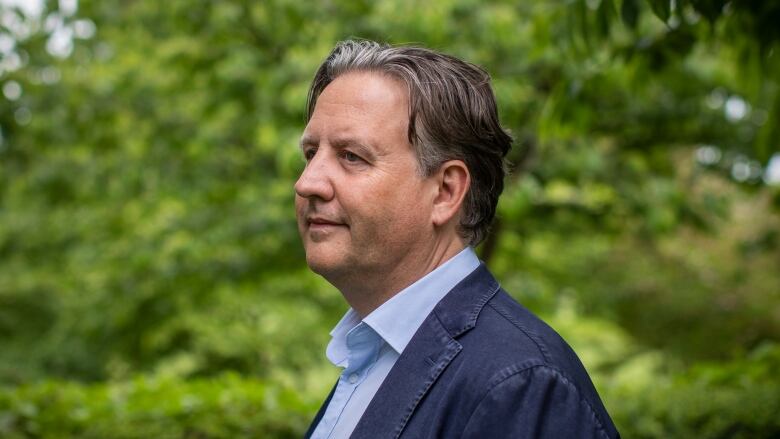 A white man with slicked-back black hair is pictured in profile.