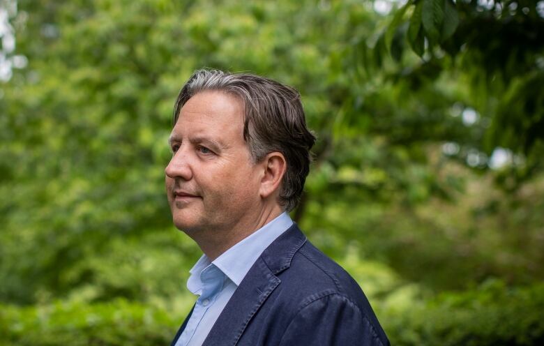 A white man with slicked-back black hair is pictured in profile.