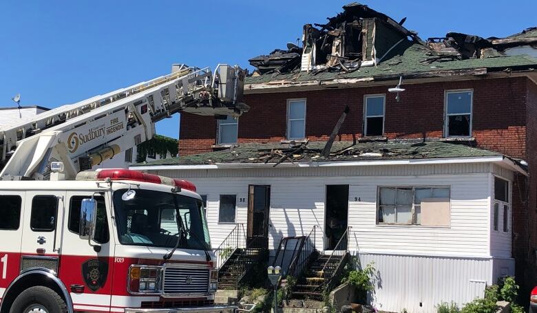 A fire truck is parked out front of a burnt out two-storey rooming house 