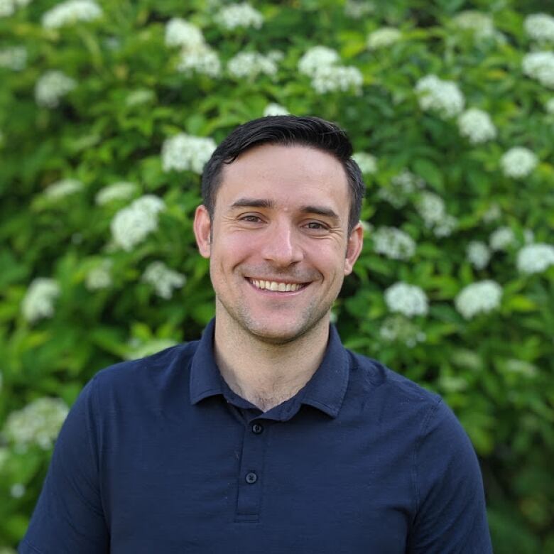 Man smiling and standing in front of green foliage.