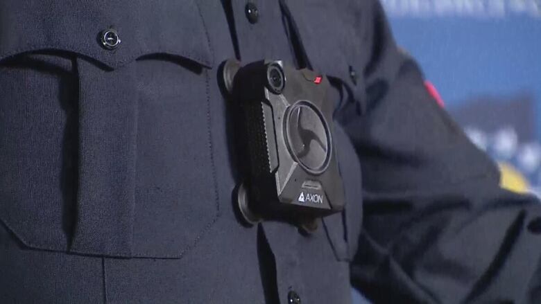 A close-up of a small black camera body sits on the chest of a uniformed police officer