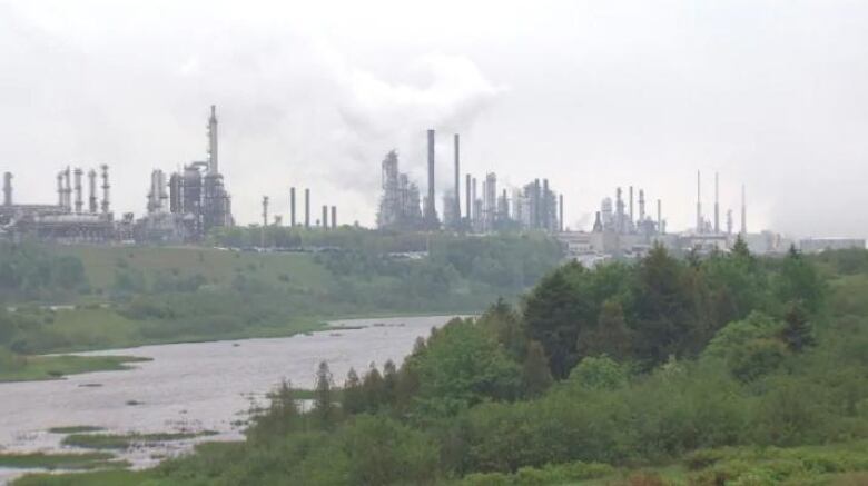 An oil refinery sits beside a river and green foliage. 