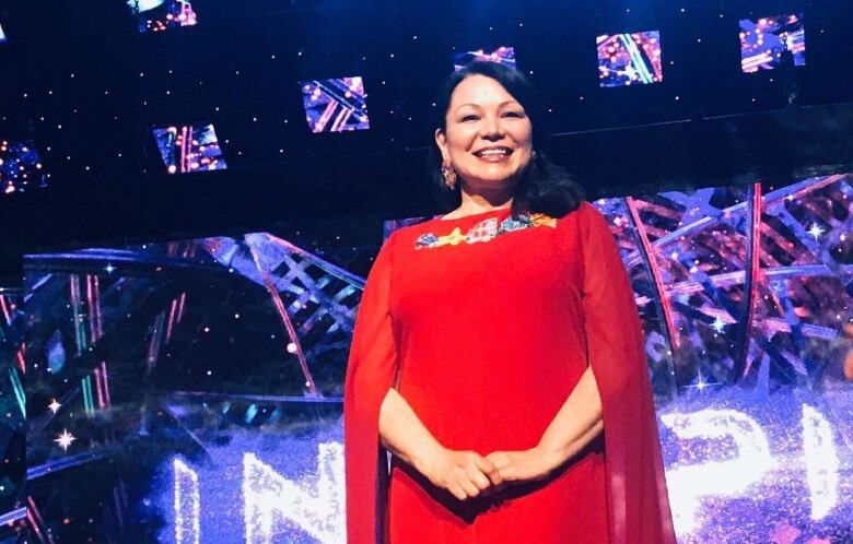 Dawn Madahbee Leach wearing a long red dress, while standing on a brightly lit stage for the Indspire Awards.