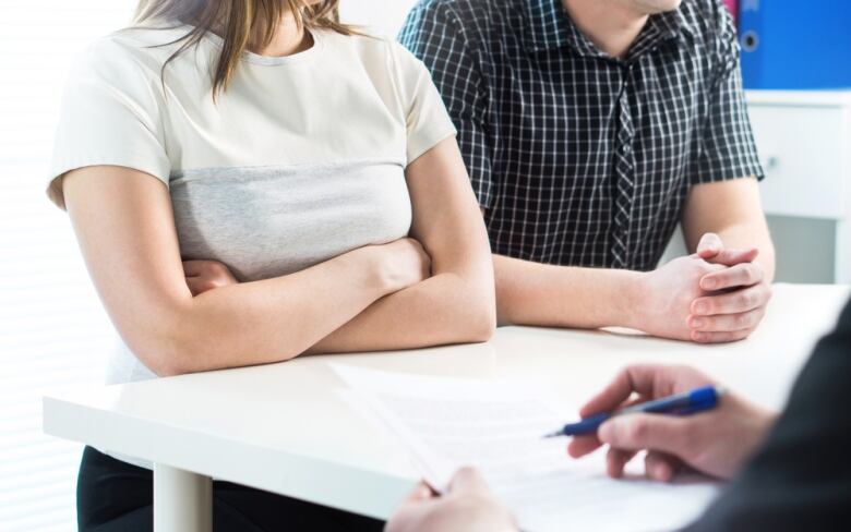 Two people seated beside each other while a third person takes notes.